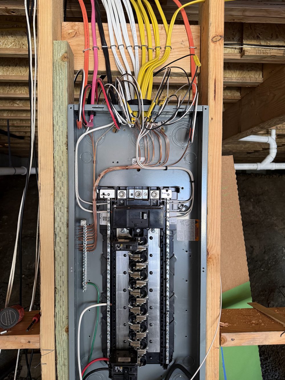 A new electrical panel set between wall studs during construction, with neat runs of yellow, white and red cable coming in from above.