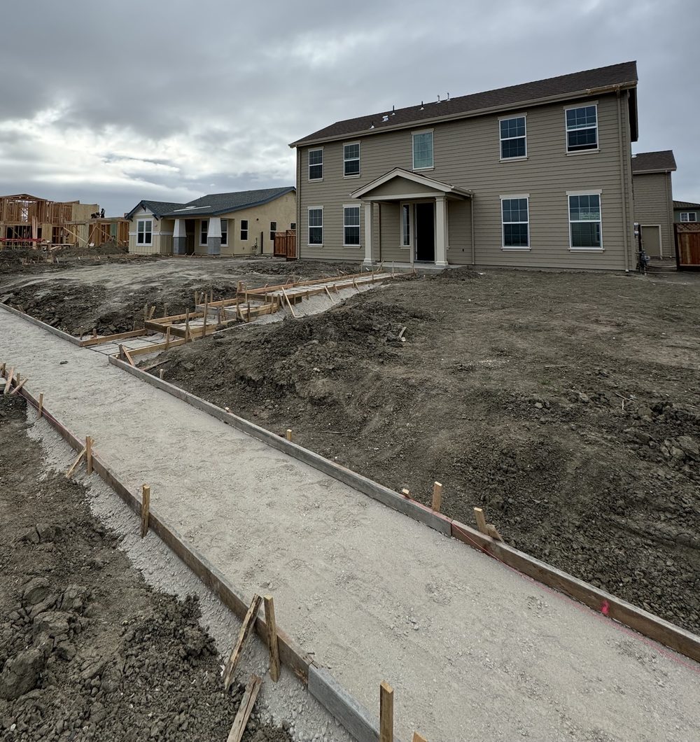 A new two-story house on a street of new construction, with sidewalk forms being set in front.